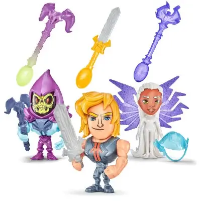 A promotional image showing three small, stylized action figures from the Masters of the Universe franchise, along with three separate, removable accessories. In the center is He-Man, a muscular man with blonde hair, holding a grey power sword. To his left is Skeletor, a purple-hooded character with a skeletal face, holding a dark grey scepter. To He-Man’s right is an angelic female character with white hair and large, sparkly purple wings, identified as ‘Teela’s new look’. Lying on the ground near her is a light blue helmet. Above the characters are three different scepter accessories: a purple and green one, a gold one, and a dark blue one. The figures are all posed as if they are ready for action. The background is a solid white.