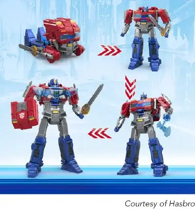 A digital photo showing four versions of a transforming Optimus Prime toy from the Transformers franchise. The top left image shows the toy in its vehicle mode, a red, blue, and grey semi-truck with wings, with a sword attached to the side. The top right image shows the toy in its robot mode, a standing Optimus Prime holding a sword. The bottom right image shows the robot in a slightly different pose, holding a blue spiked mace. Red arrows point between the different forms, indicating the transformation process. The bottom left image shows a more detailed view of the robot, holding a sword and a red shield. The background is a blue and white landscape. The bottom right corner has a caption that reads ‘Courtesy of Hasbro’.