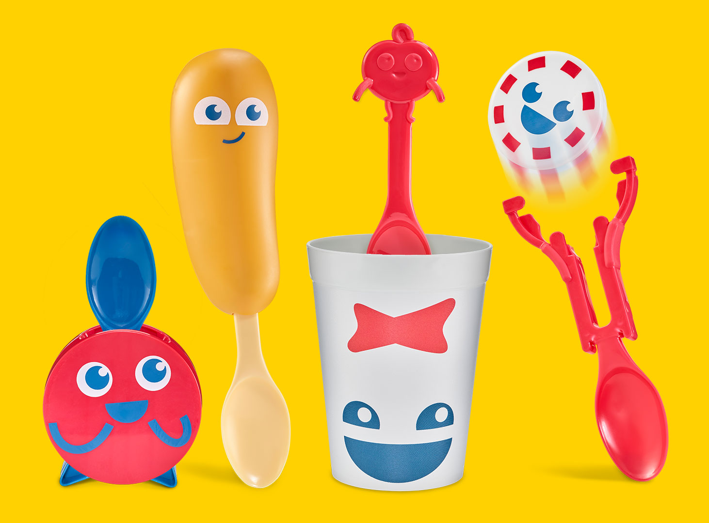 A set of Sonic Wacky Pack toys with food-themed characters. A red button-shaped toy with a spoon handle, a smiling corndog figure with spoon attached, a white drink cup with a red bowtie face containing a spoon topped with a red button character, and a red spoon toy launching a peppermint disc character.