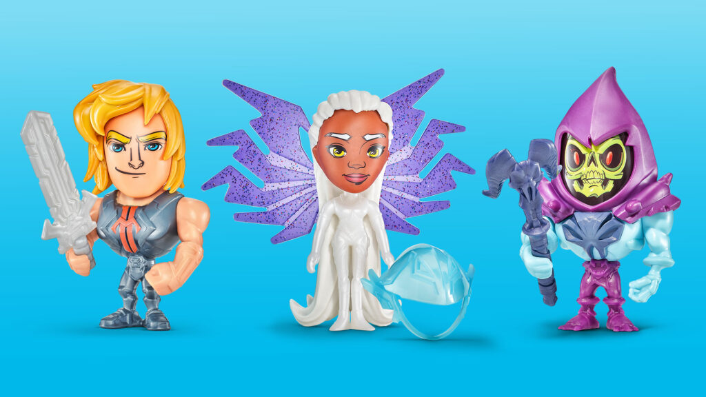 Three small collectible figurines from Masters of the Universe. On the left, a muscular He-Man figure with blond hair holding a gray sword. In the center, a white-robed female character with large purple glittery wings and a separate blue accessory. On the right, a Skeletor figure with a green skull face, purple hood, and purple staff.