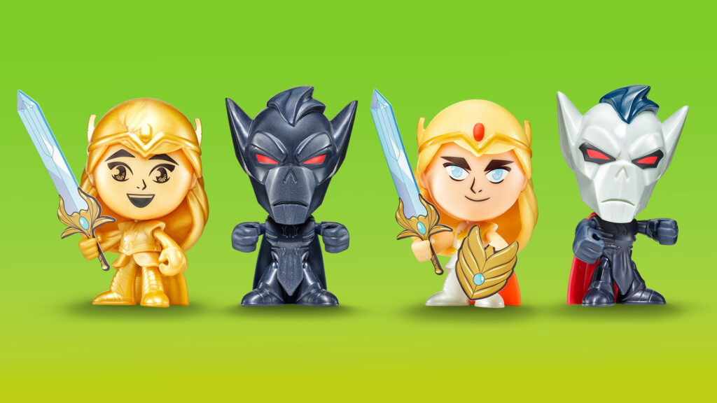 Four small She-Ra collectible figures in stylized cartoon form. Two golden She-Ra characters with swords are paired with two villain figures: black armored character with red eyes and a gray-skinned character with a blue mohawk and red cape.