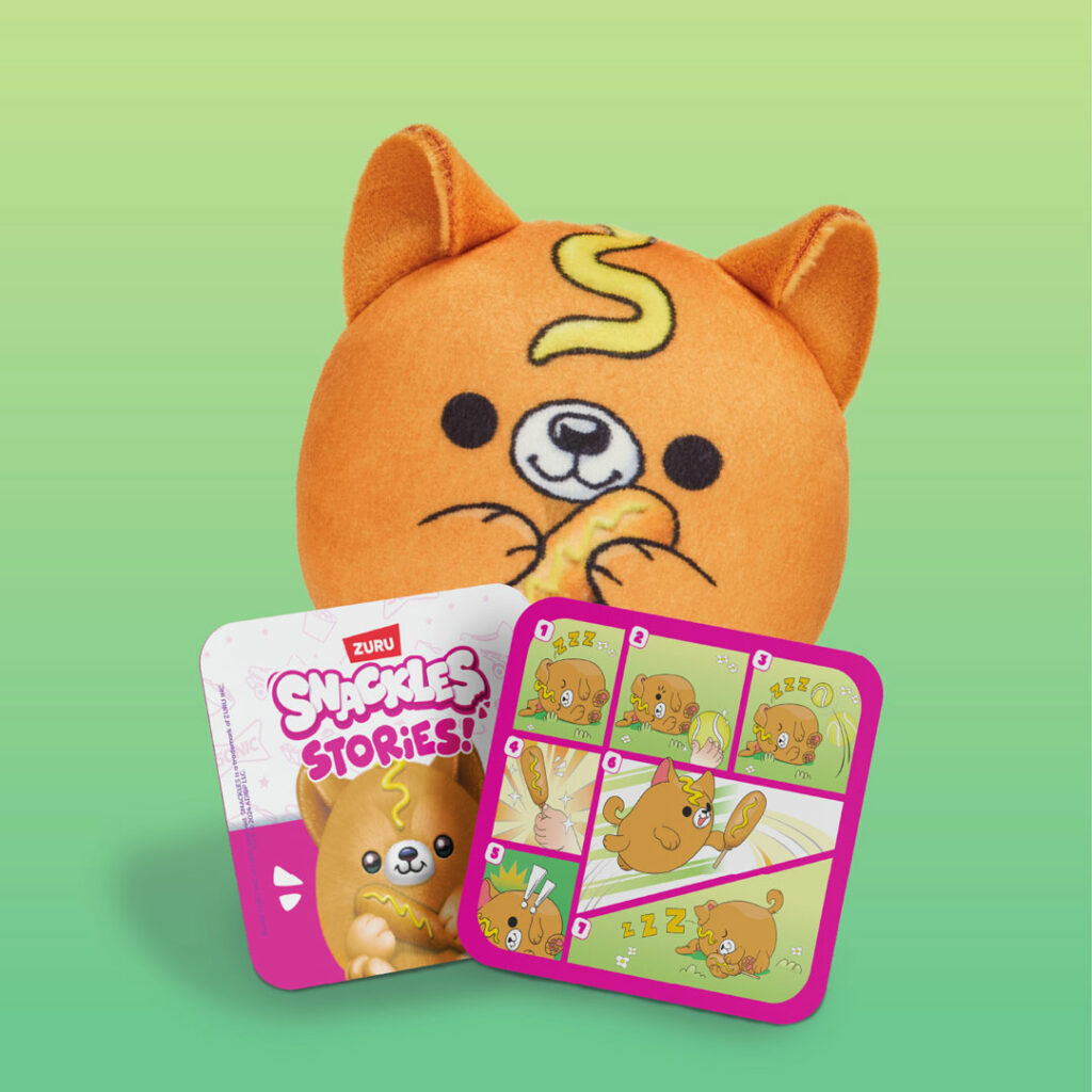 An orange corndog-inspired dog plush with a yellow swirl on its forehead, holding a Sonic corn dog. Two cards are in front: one shows the character illustration with “Snackles Stories” text, and the other depicts a six-panel comic strip of the dog sleeping, waking, and enjoying a corn dog snack.