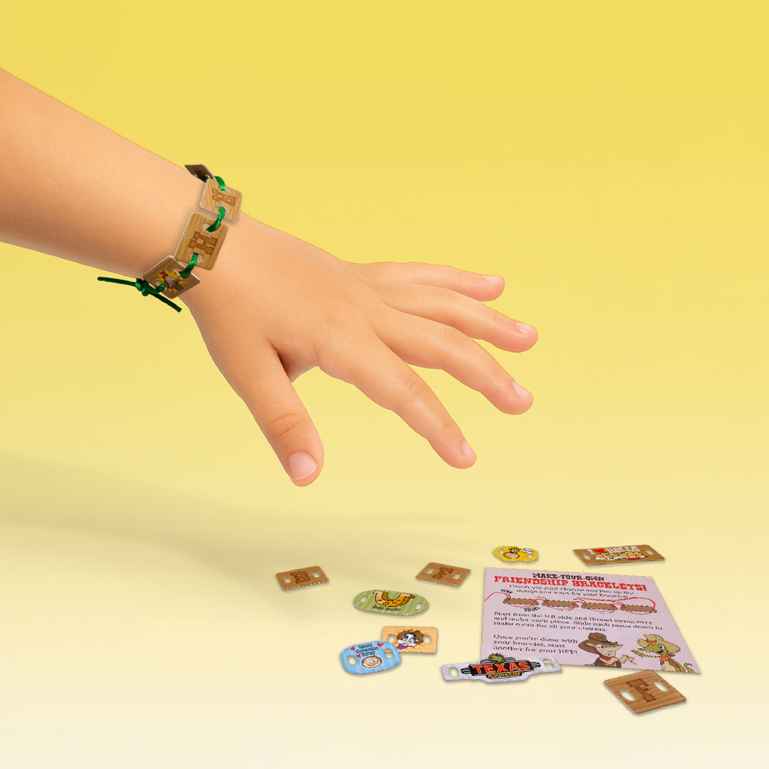 A child’s hand wearing a completed bracelet made from the kit, shown next to several loose charms and an instruction card.