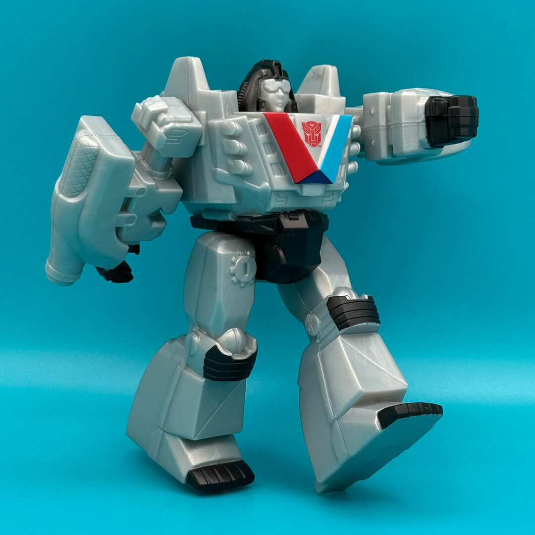The Valvotron figure posed mid-stride, as if walking, with one arm extended forward. The teal background emphasizes the gray, black, and chest emblem colors.